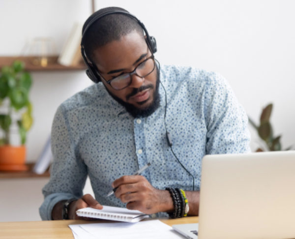 Focused,African,Business,Man,In,Headphones,Writing,Notes,In,Notebook